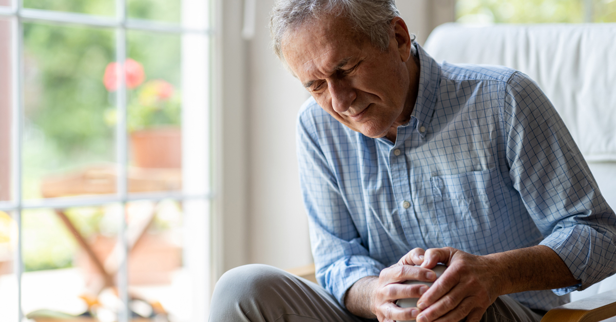 A man wincing in pain and holding his knee