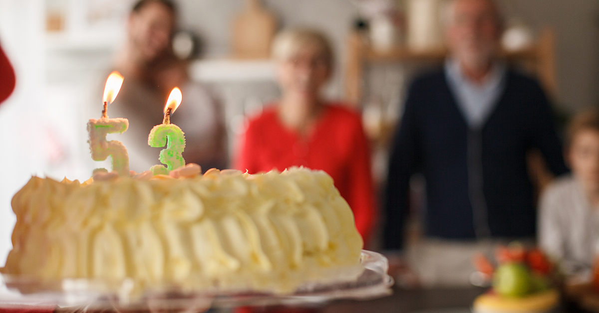 Birthday cake with 53 candles in the foreground and people in the background