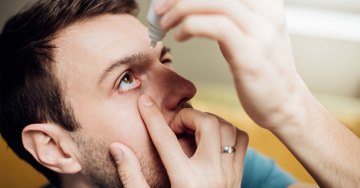 Man putting eye drops in his eyes