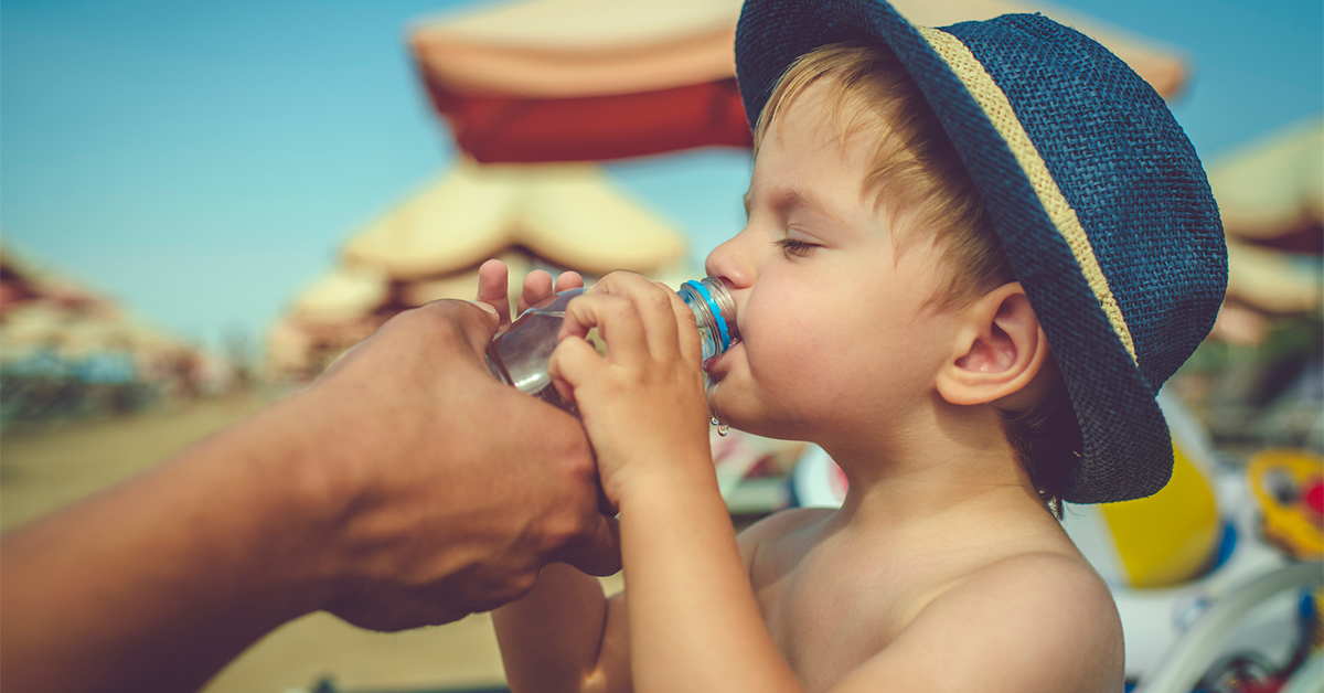 Child drinking water on the beach on summer