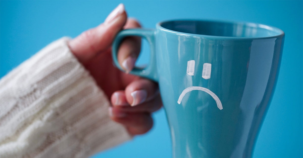 Close-up of a female hand in a white sweater holds a blue cup with a sad smiley